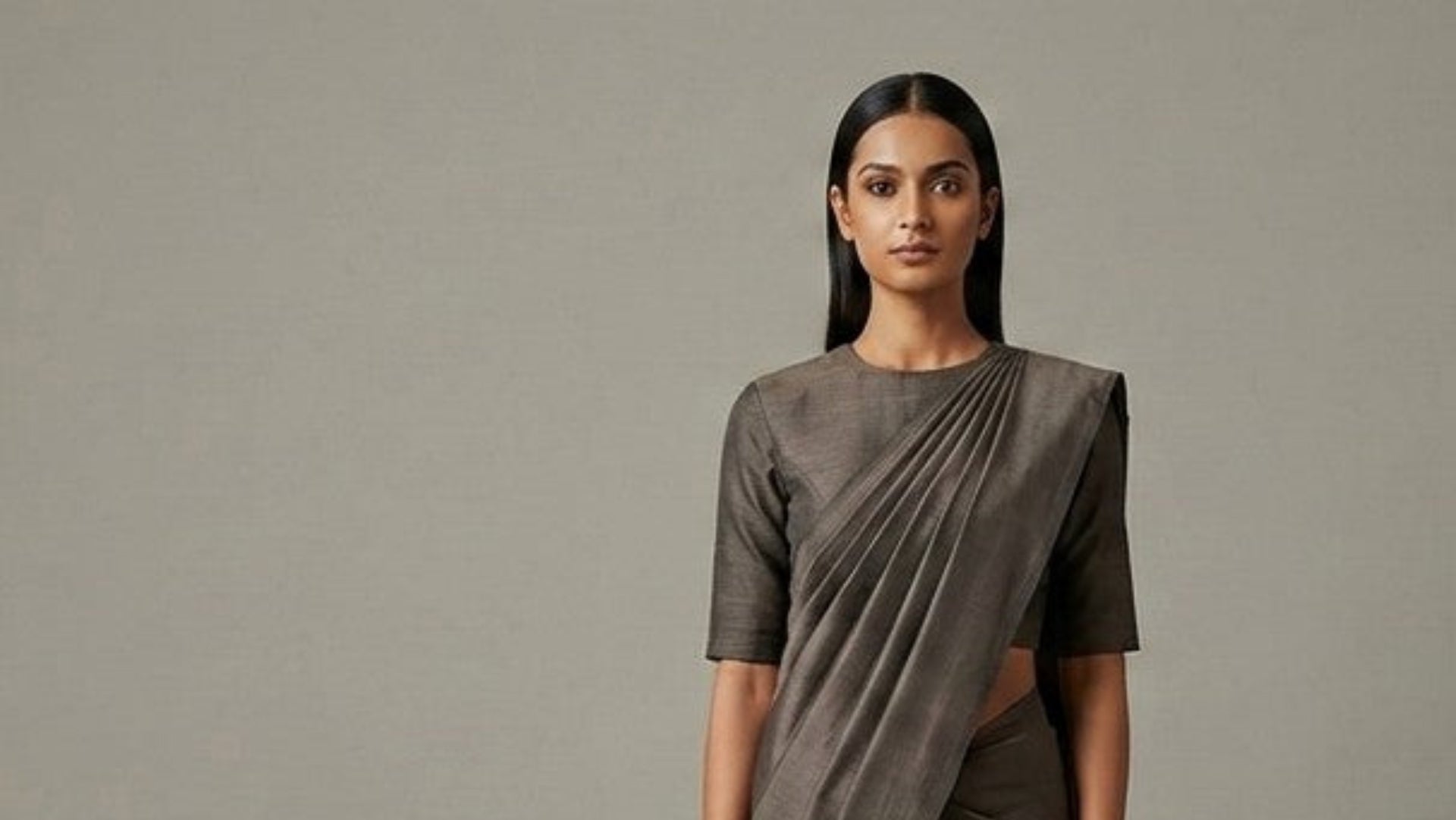 Modern Indian woman wearing a structured handwoven silk saree in a minimalist studio setting.